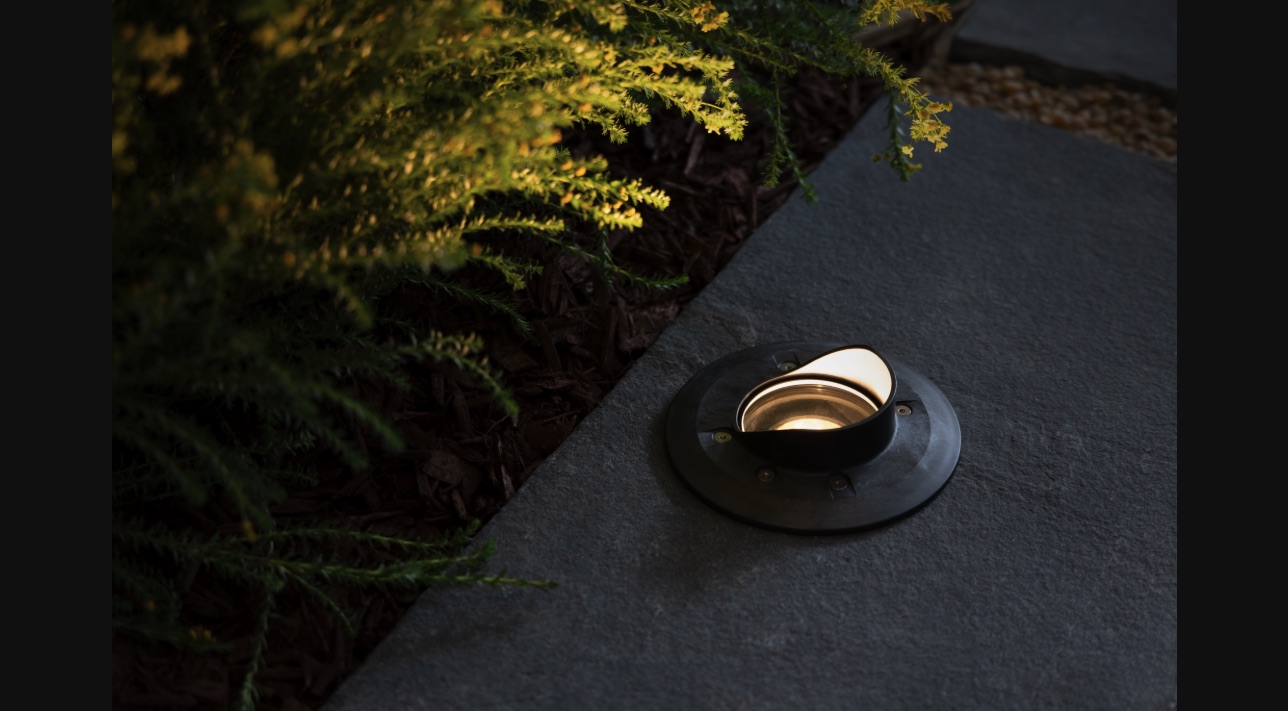 FX Luminaire Terra TN-61 cowling in-grade light installed flush in a stone paver, washing a shrub at night